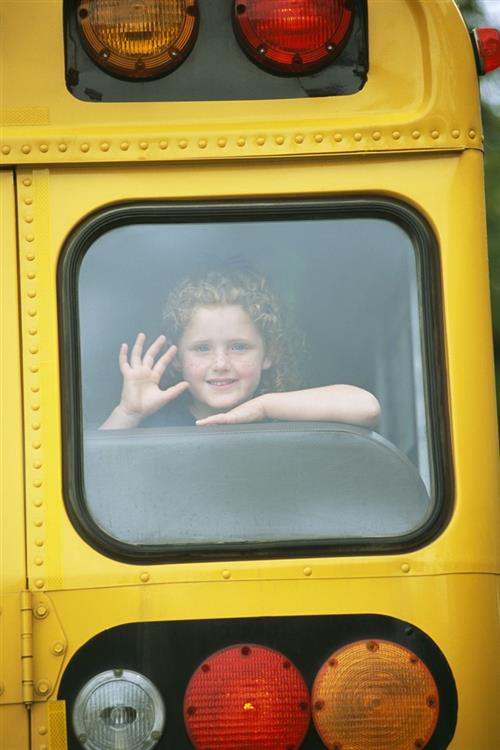 Smiling child waving through bus window 